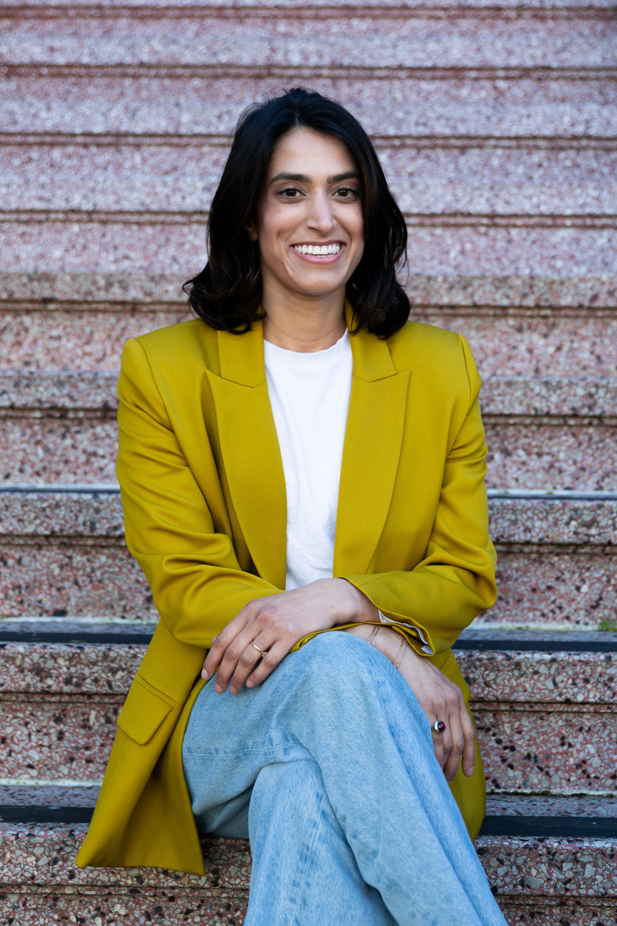 Darshini Patel sitting on steps in a yellow-green blazer